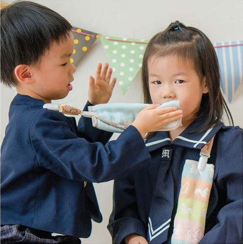 孩子拿淺藍色六重紗小手帕替另一個孩子擦嘴,手帕以短夾固定在衣服上