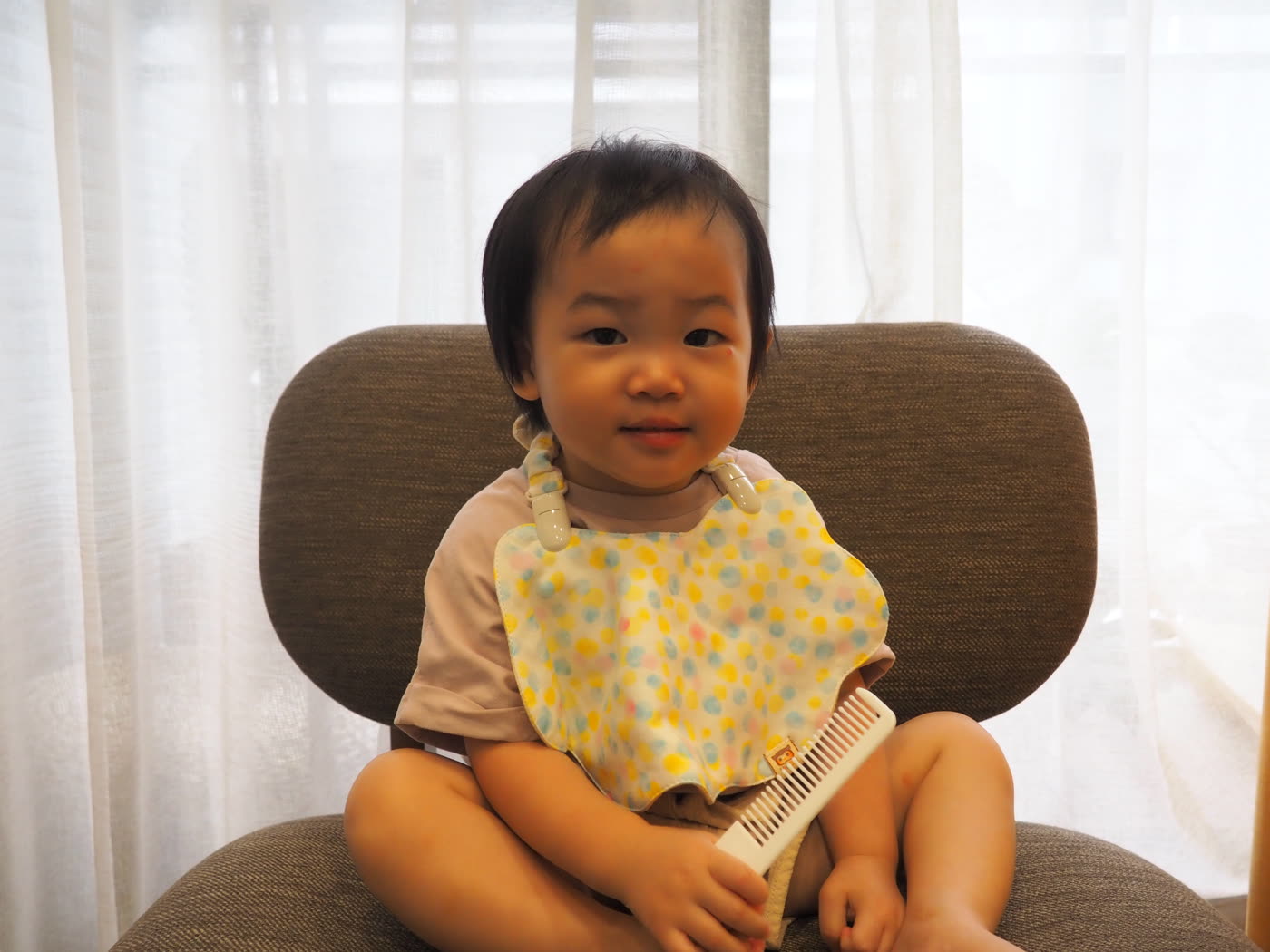 幼兒坐在椅子上，胸前戴著水果泡泡糖花色的雲朵波浪圍兜，兩個白色夾子夾在肩口